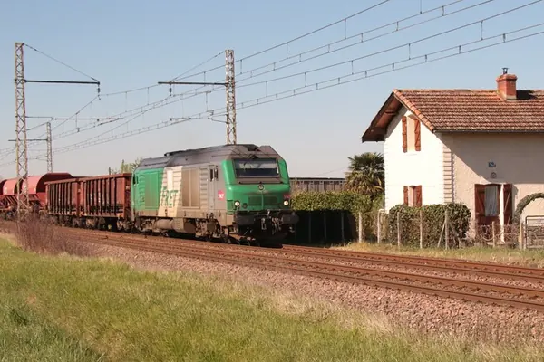 Train de fret SNCF passant le long d’une maison, près de la voie