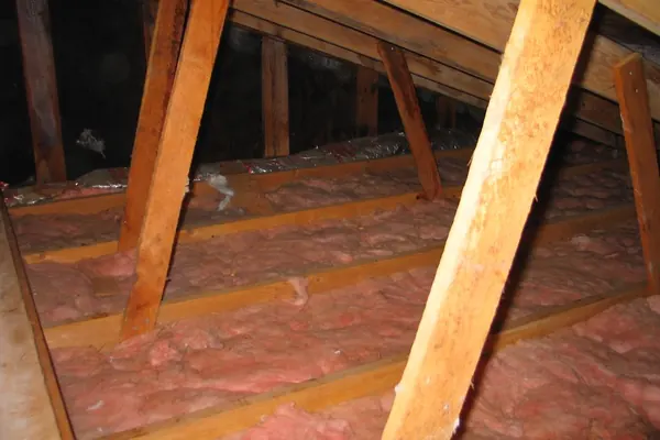 Combles d’une maison avec une couche d’isolant ancienne et mince entre les solives