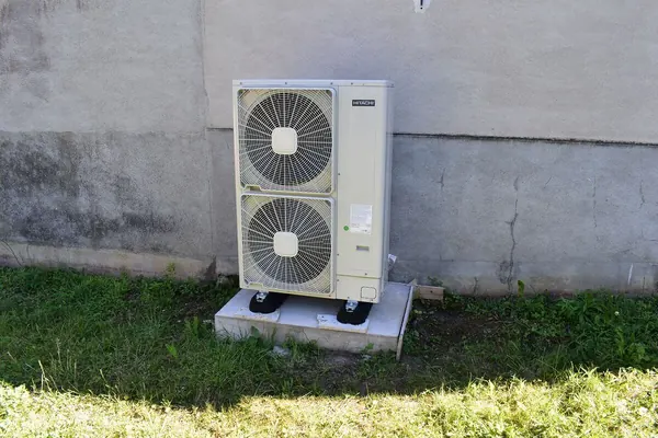 Unité extérieure d’une pompe à chaleur air-eau posée sur des plots, contre le mur d’une maison du Tarn